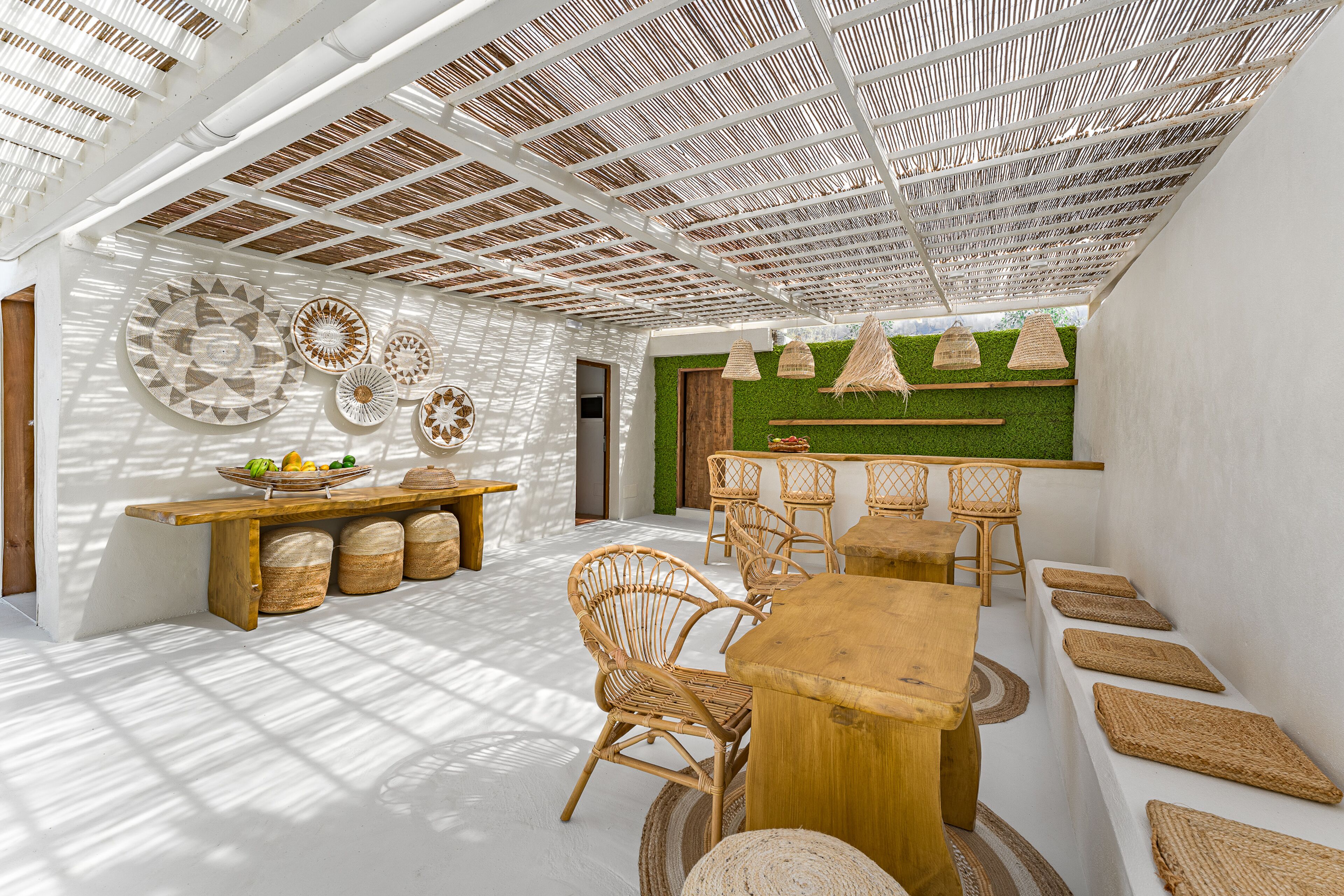Une pièce spacieuse et bien éclairée, avec un plafond haut, une table à manger en bois, des chaises en osier et un petit coin bar avec des tabourets.