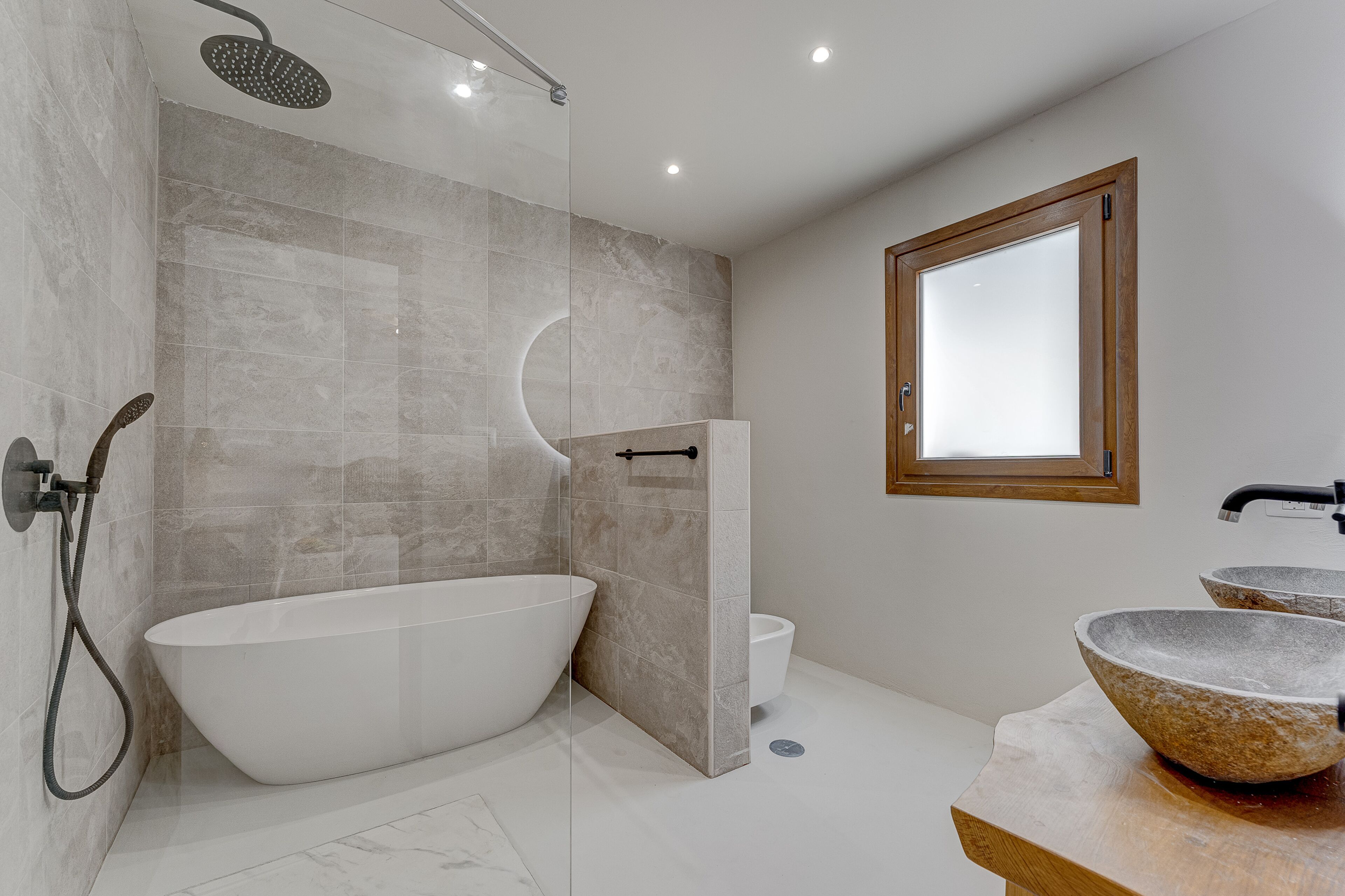 Een moderne badkamer met een vrijstaand bad, een douche met glazen wanden en een raam met houten kader.