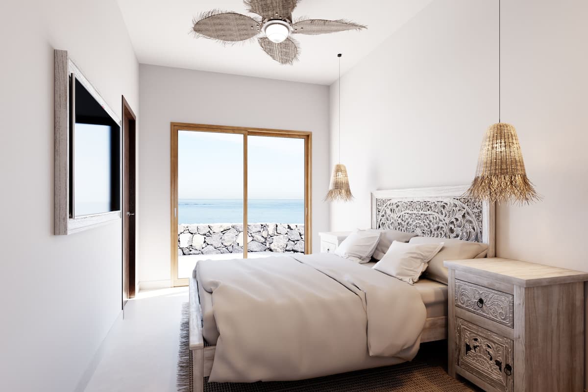 Une chambre avec un grand lit, une table de chevet, une lampe en osier et une vue sur la mer par une porte vitrée.