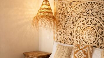 A bedroom with a bed, a hanging light fixture, a decorative headboard, and a bedside table.