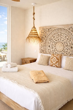 A bedroom with a large bed, a decorative headboard, a hanging light fixture, and a view of the outdoors. - Costa Mágica – Romantic Ocean Boutique Hotel &amp; Club (San Cristóbal de La Laguna)