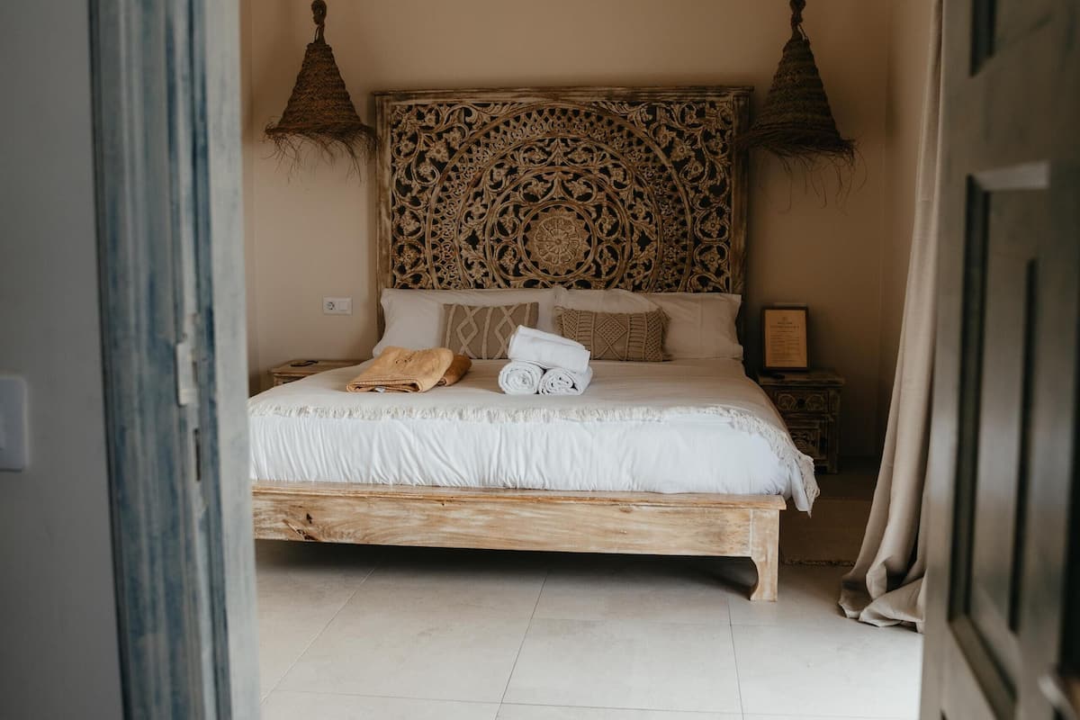 Une chambre à coucher avec un lit en bois, un ventilateur de plafond, une tête de lit à motifs et une table de chevet avec une lampe.