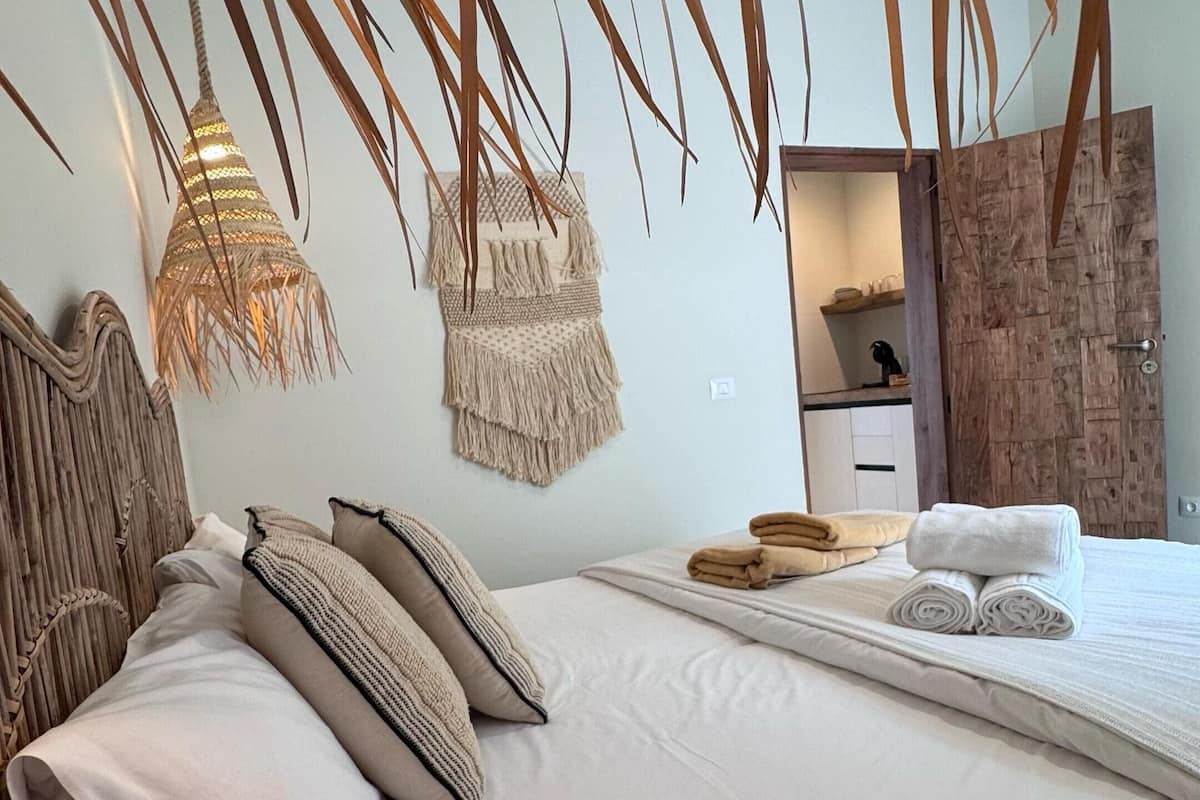 Un lit bien fait, avec du linge de lit blanc et une tête de lit en bois, une armoire en bois et un luminaire en macramé fixé au mur.