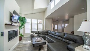 A spacious living room with a large sectional sofa, a flat-screen TV mounted on the wall, and a potted plant.