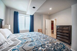 A bedroom with a bed, a dresser, a window with curtains, and a door leading to a bathroom.