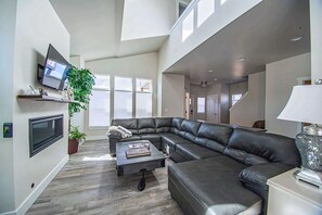 A modern living room with a sectional sofa, a flat-screen TV mounted on the wall, and a potted plant.