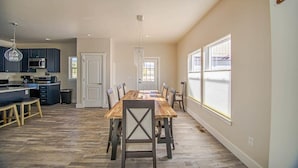 A spacious kitchen with dark cabinets, a dining area with a wooden table and chairs, and large windows providing natural light.