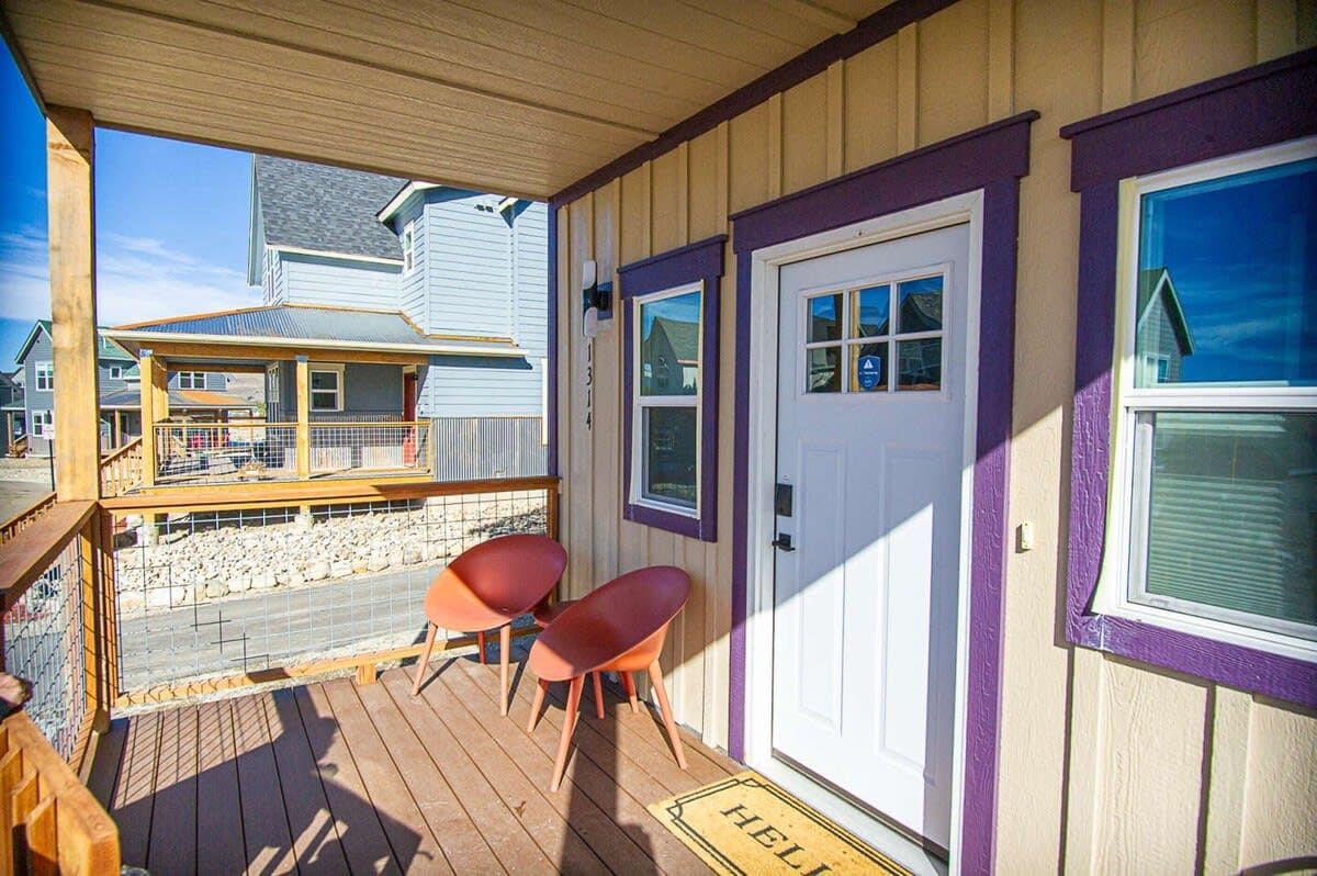 A covered porch with two chairs, a door, and a view of the beach.