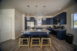 Una cocina moderna con armarios oscuros, una isla central con taburetes altos e iluminación colgante.