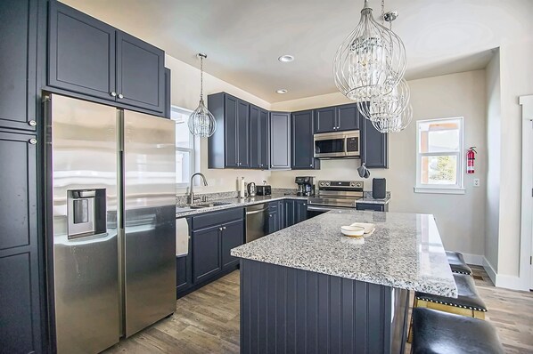 A modern kitchen with dark cabinetry, stainless steel appliances, a granite countertop, and pendant lighting.