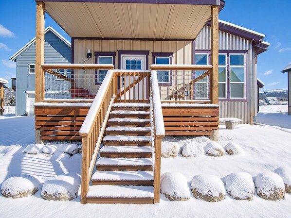 A wooden staircase leading to a covered porch with a view of a snowy landscape.
