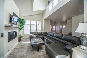 Una sala de estar amplia con un sofá modular grande, un televisor de pantalla plana montado en la pared y una planta en maceta.
