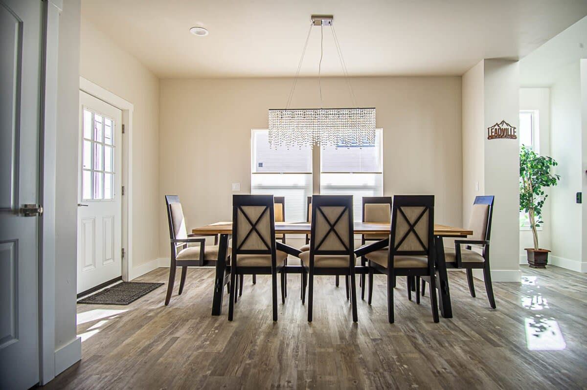 A dining area with a wooden table and chairs, a hanging light fixture, and a window with blinds.