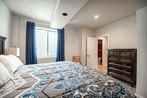 Un dormitorio con cama, cómoda, ventana con cortinas y puerta que da a otra habitación.