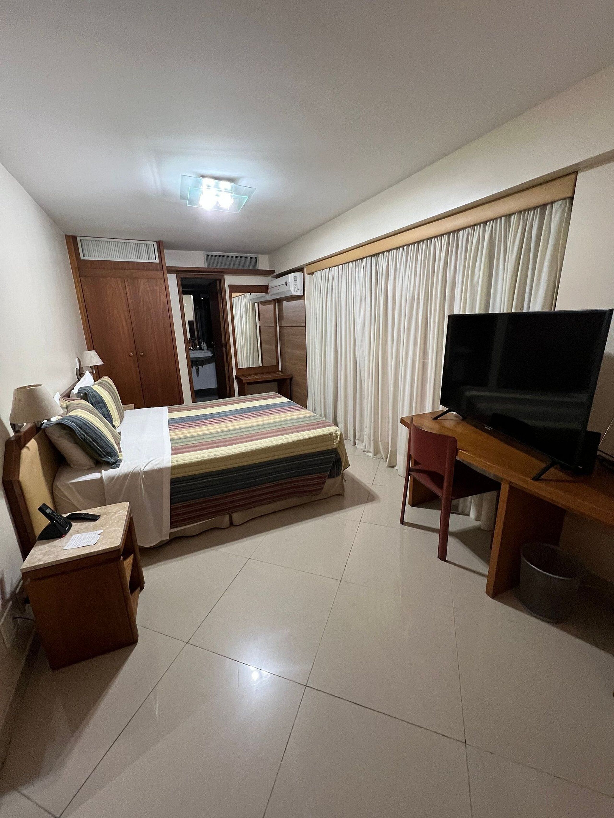 A hotel room with a bed, a desk with a TV, a wardrobe, and a bathroom visible through an open door.