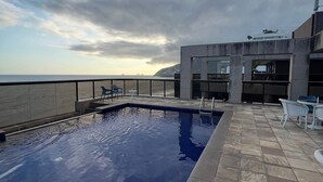 A swimming pool with a view of the sea, a patio area with chairs, and a modern building structure. - Flat Ipanema - Vieira Souto 500 (Rio de Janeiro)