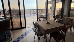 A dining area with a view of the sea, featuring tables and chairs, a pool, and a balcony. - Flat Ipanema - Vieira Souto 500 (Rio de Janeiro)