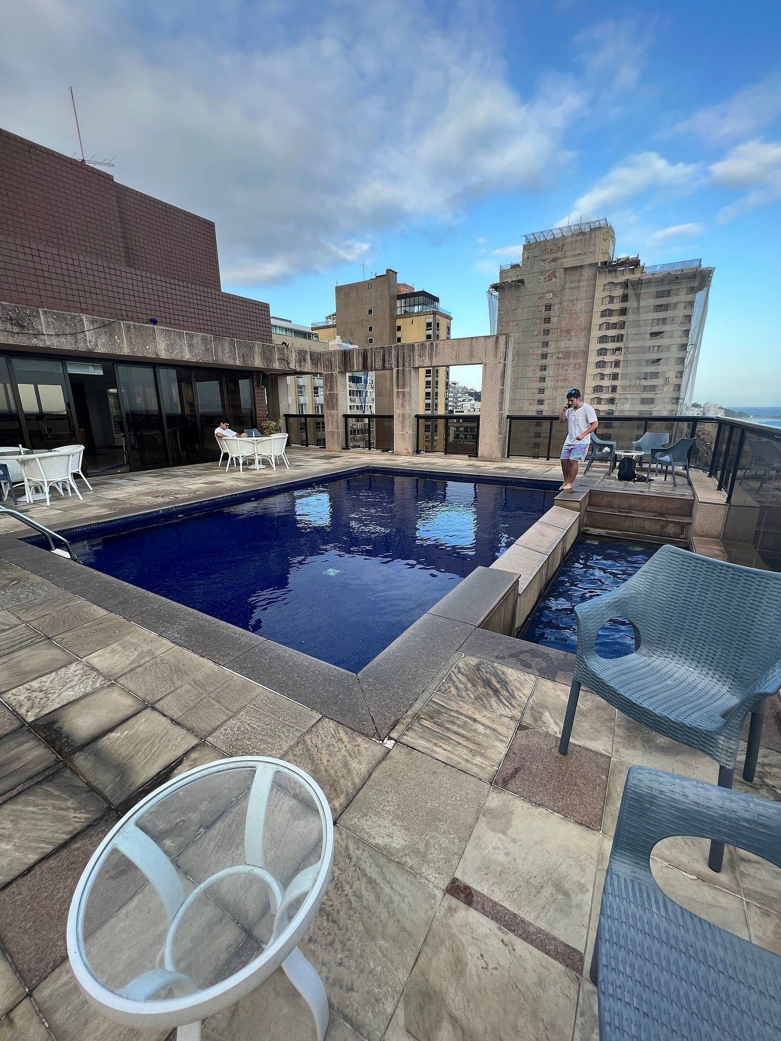 A rooftop pool area with a clear view of the cityscape, including high-rise buildings and a distant coastline.