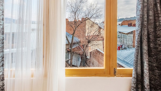 Una stanza con una grande finestra, pavimento in legno e vista su edifici e alberi.