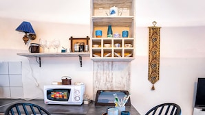 Una cucina compatta con un tavolo da pranzo, due sedie, un forno a microonde e uno scaffale con stoviglie e un oggetto decorativo.