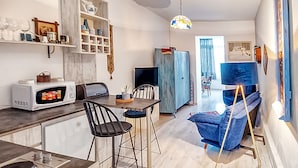 Una cucina moderna con forno a microonde, sgabelli da bar e un tavolo da pranzo. Si vede un divano blu e un quadro appeso al muro.