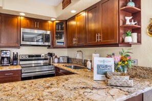 A kitchen with wooden cabinets, stainless steel appliances, granite countertops, and a decorative sign.