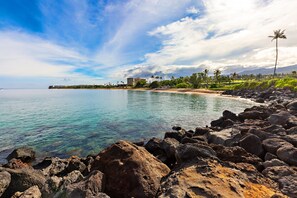 A coastal landscape with clear water, rocky shoreline, and a distant building.