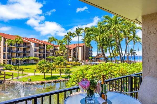 A hotel balcony with a view of a pool, palm trees, and a building with a red roof.