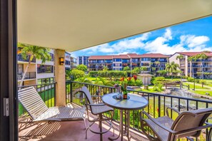 A balcony with outdoor furniture, a small table with a bottle, and a view of a hotel complex with multiple buildings and a garden.