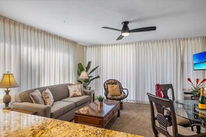 A living room with a sofa, armchair, coffee table, and a dining table with chairs.