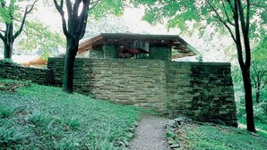 Un bâtiment en pierre doté d’un toit en pente, entouré d’arbres et d’une zone herbeuse.