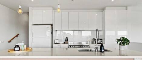 Uma cozinha moderna com armários brancos, uma ilha central e iluminação pendente.