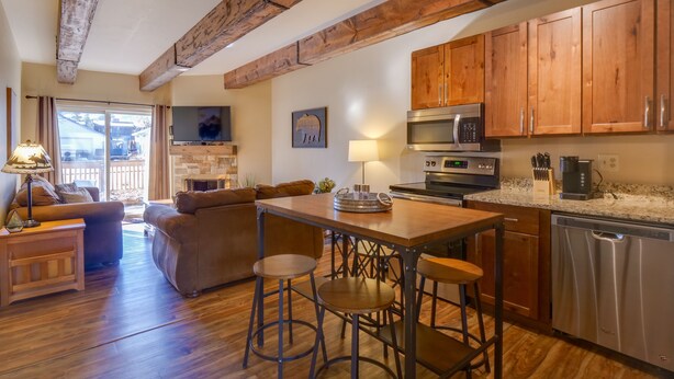 A modern kitchen with wooden cabinets, a dining area with stools, and a living room with a sofa and a TV. - 2 Bd 1.5 Ba Condo close to main street in Frisco, CO! (Frisco)