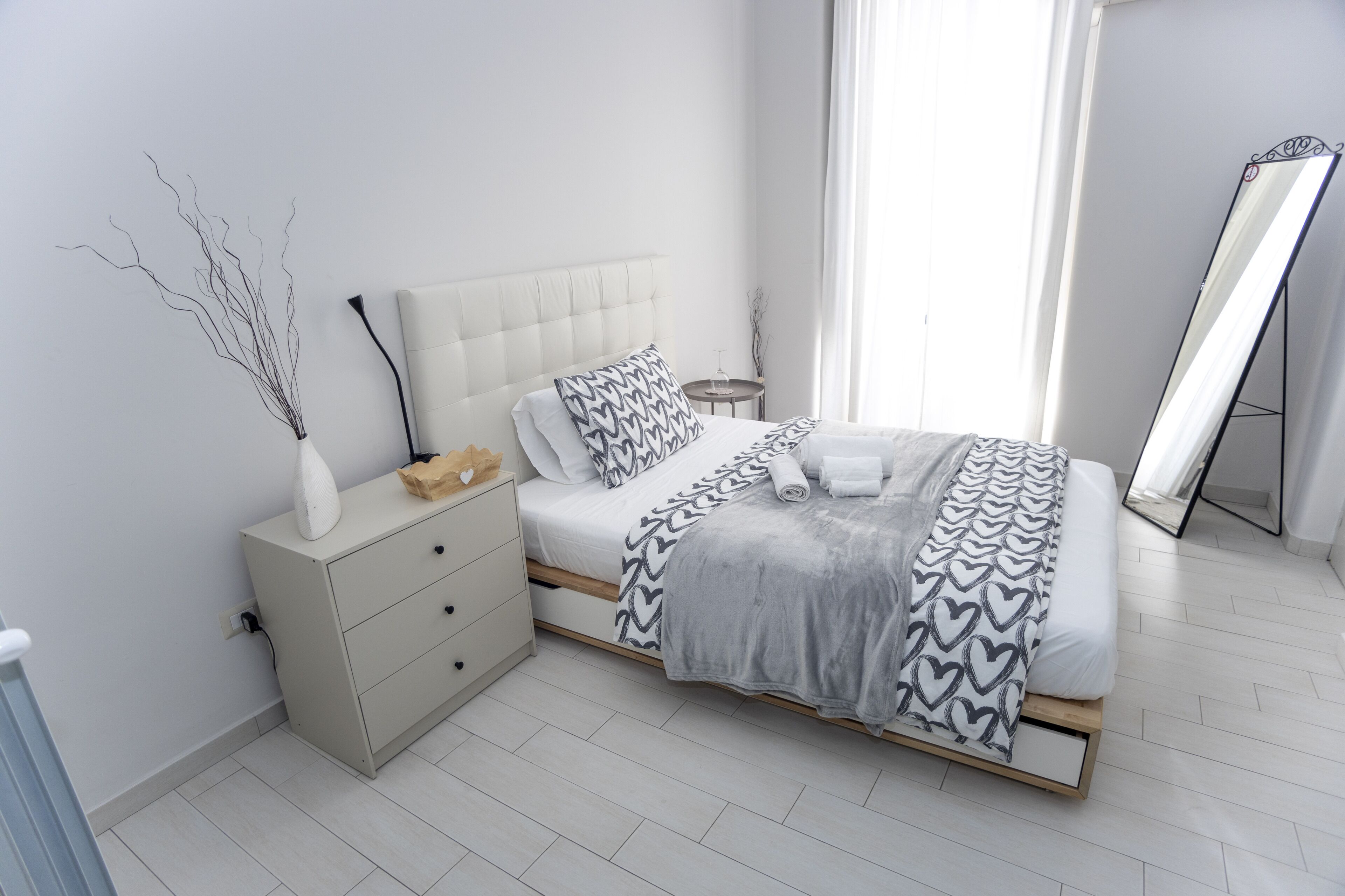 A modern bedroom with a bed, bedside table, and a mirror.