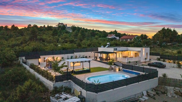 Une maison moderne dotée d’une piscine, d’un patio couvert et offrant une vue sur la forêt environnante.