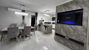 Un espace de repas moderne avec un téléviseur à écran plat fixé au mur, une table à manger avec des chaises, et une cuisine en arrière-plan.
