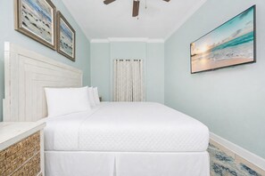 A bedroom with a bed, a ceiling fan, a large window with curtains, and artwork on the walls.
