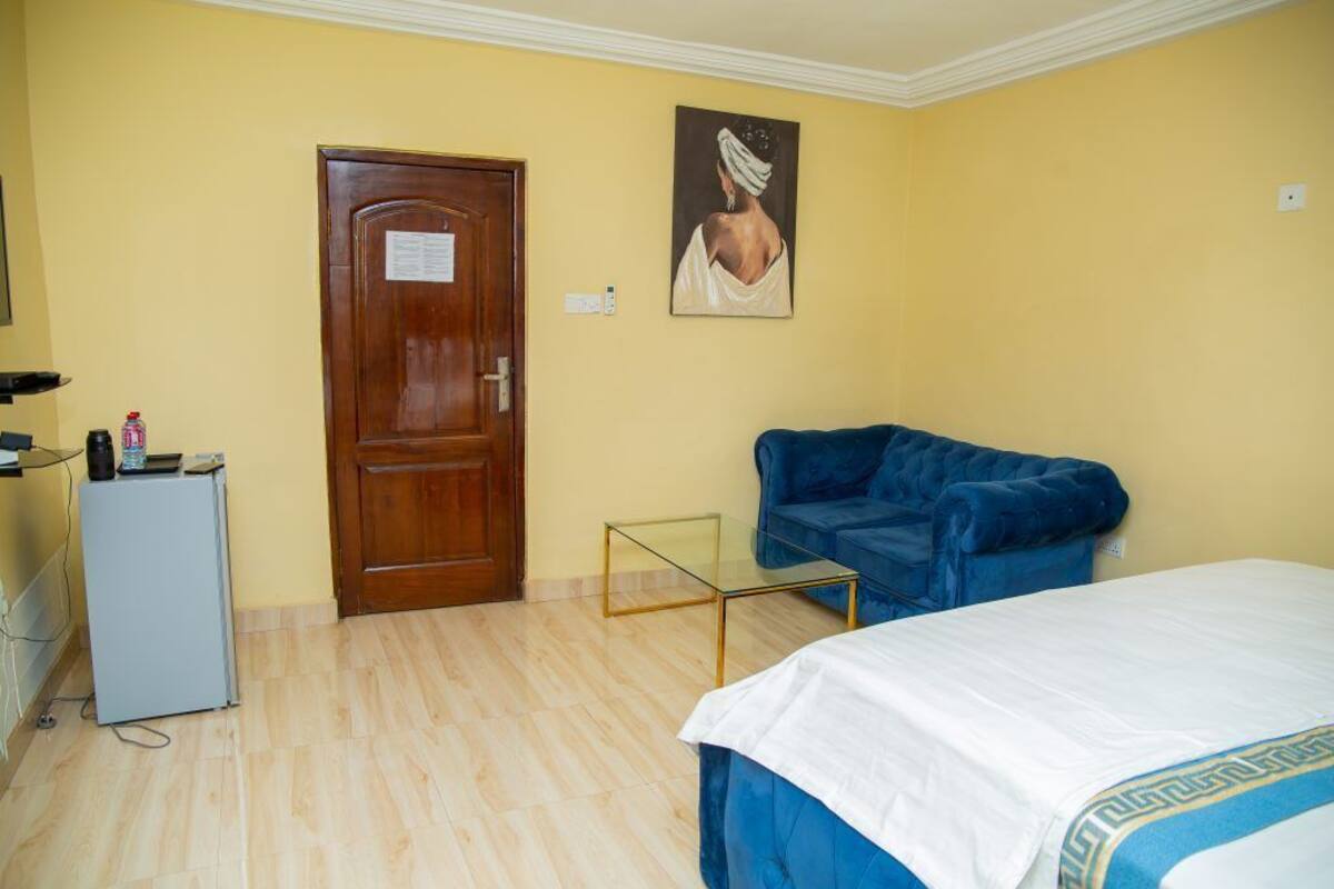 A room with a bed, a blue sofa, a small table, a door, and a painting on the wall.