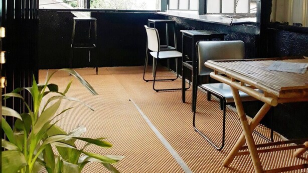 Ein Restaurant mit hoher Decke, Metallwänden und großen Fenstern. Tische und Stühle sind zum Essen bereitgestellt.