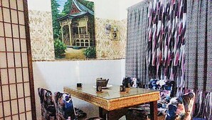 Ein Essbereich mit einem Holztisch und Korbstühlen, einem Bild eines traditionellen Gebäudes an der Wand und einem gemusterten Vorhang.