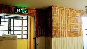 Ein Zimmer mit Backsteinwand, einem Fenster mit Metallgitter und einer Tür mit grünem Ausgangsschild.