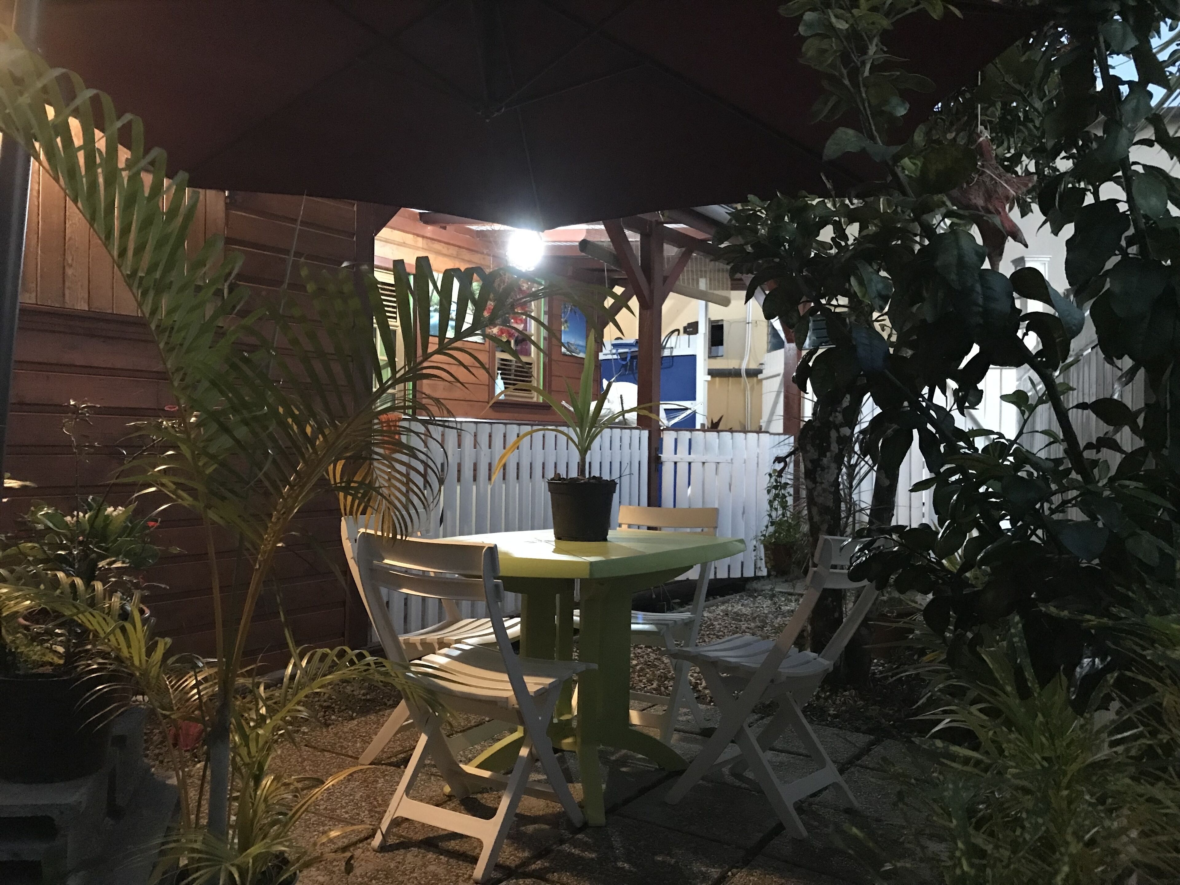 Ein Terrassenbereich im Freien mit Tisch und Stühlen, umgeben von Blumentöpfen und einem Holzzaun.