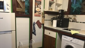 Kompakti keittiö, jossa on jääkaappi, mikroaaltouuni, kahvinkeitin ja pesukone.