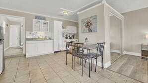 A modern kitchen with white cabinets, a dining area with a wooden table and metal chairs, and a painting on the wall.
