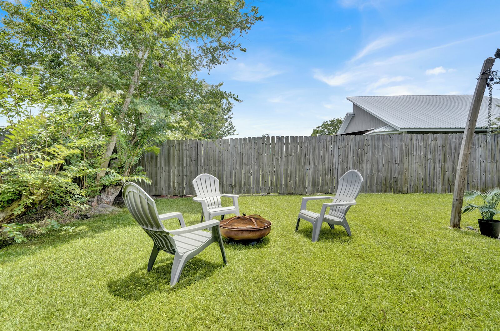 Un jardin avec deux chaises Adirondack blanches, un bateau en bois et une clôture en bois.