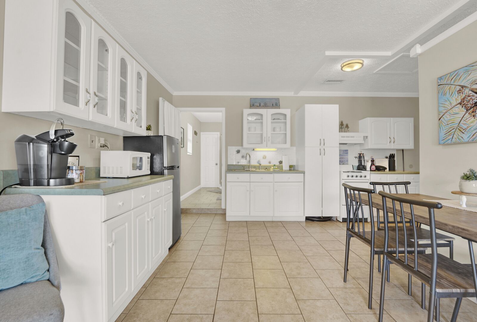 A modern kitchen with white cabinetry, a central island, and a dining area with bar stools.