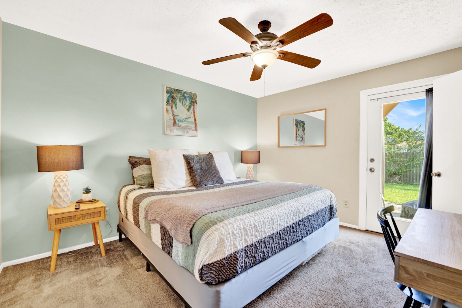 Une chambre à coucher comprenant un lit, deux tables de chevet avec des lampes, un ventilateur de plafond et une porte donnant sur un balcon.