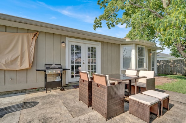 Un patio exterior con una parrilla, muebles de mimbre y una zona cubierta.