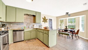A kitchen with green cabinets, a dishwasher, and a dining area with a table and chairs.