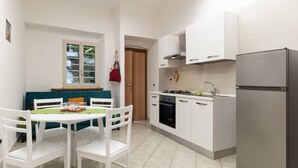Cocina compacta con armarios blancos, refrigerador de acero inoxidable y comedor con mesa y sillas.